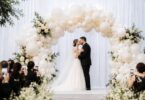 A garden-style wedding balloon arch woven with trailing eucalyptus and soft ivory balloons framing a ceremony aisle