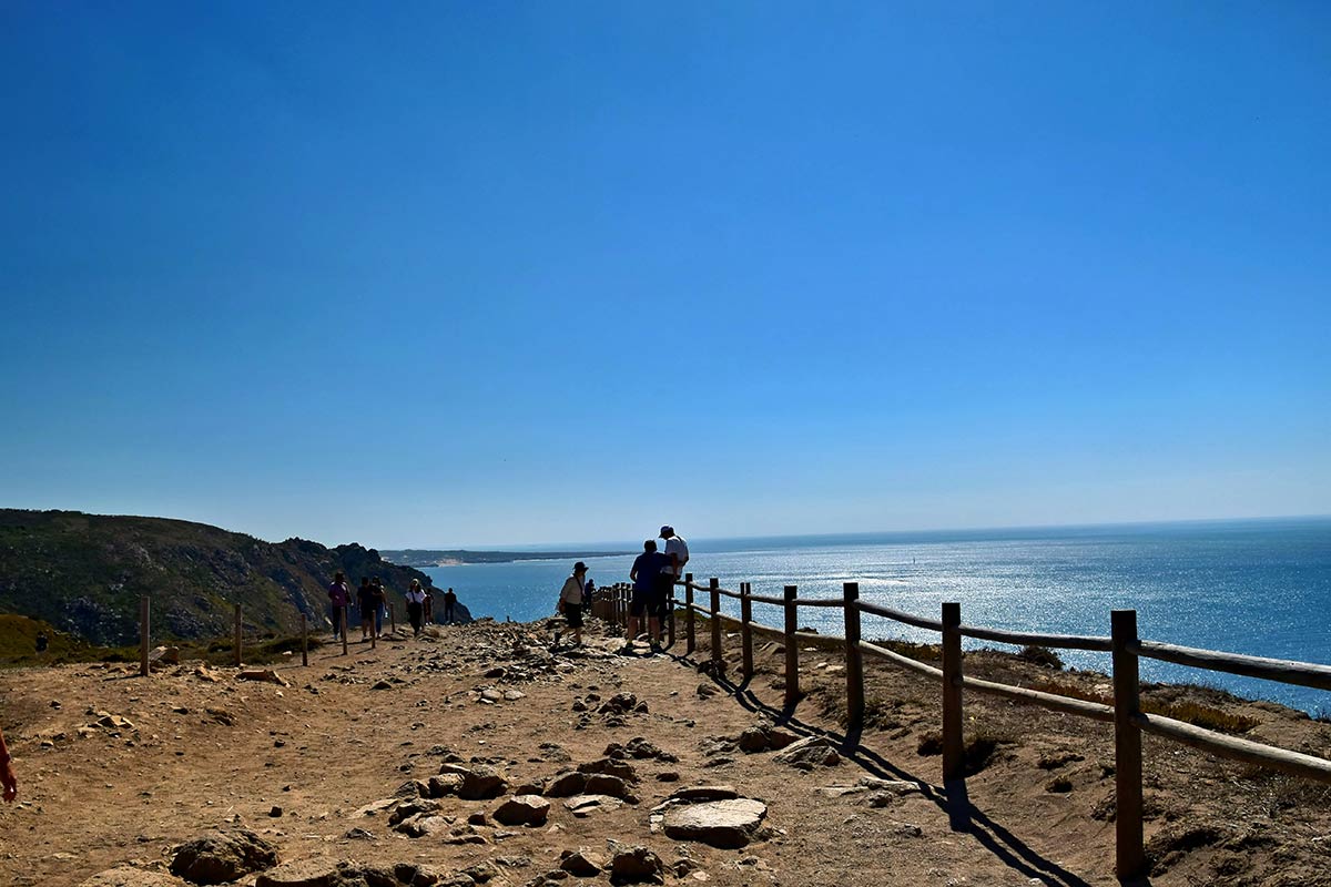 Walkers pausing at a fenced clifftop viewpoint above the Atlantic on the Portuguese coast